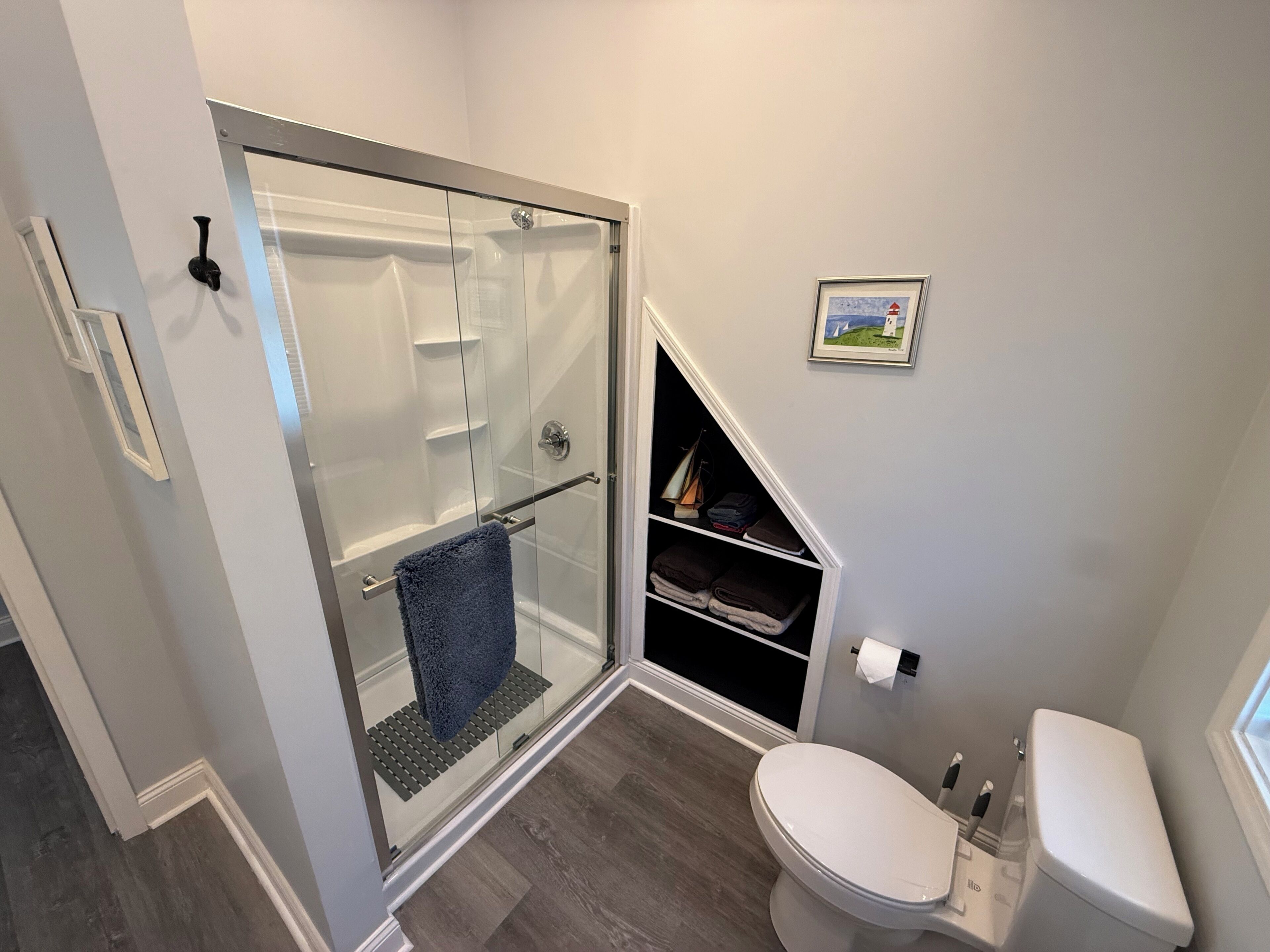 Une salle de bain avec une douche à parois de verre, des toilettes blanches et une étagère avec des serviettes.