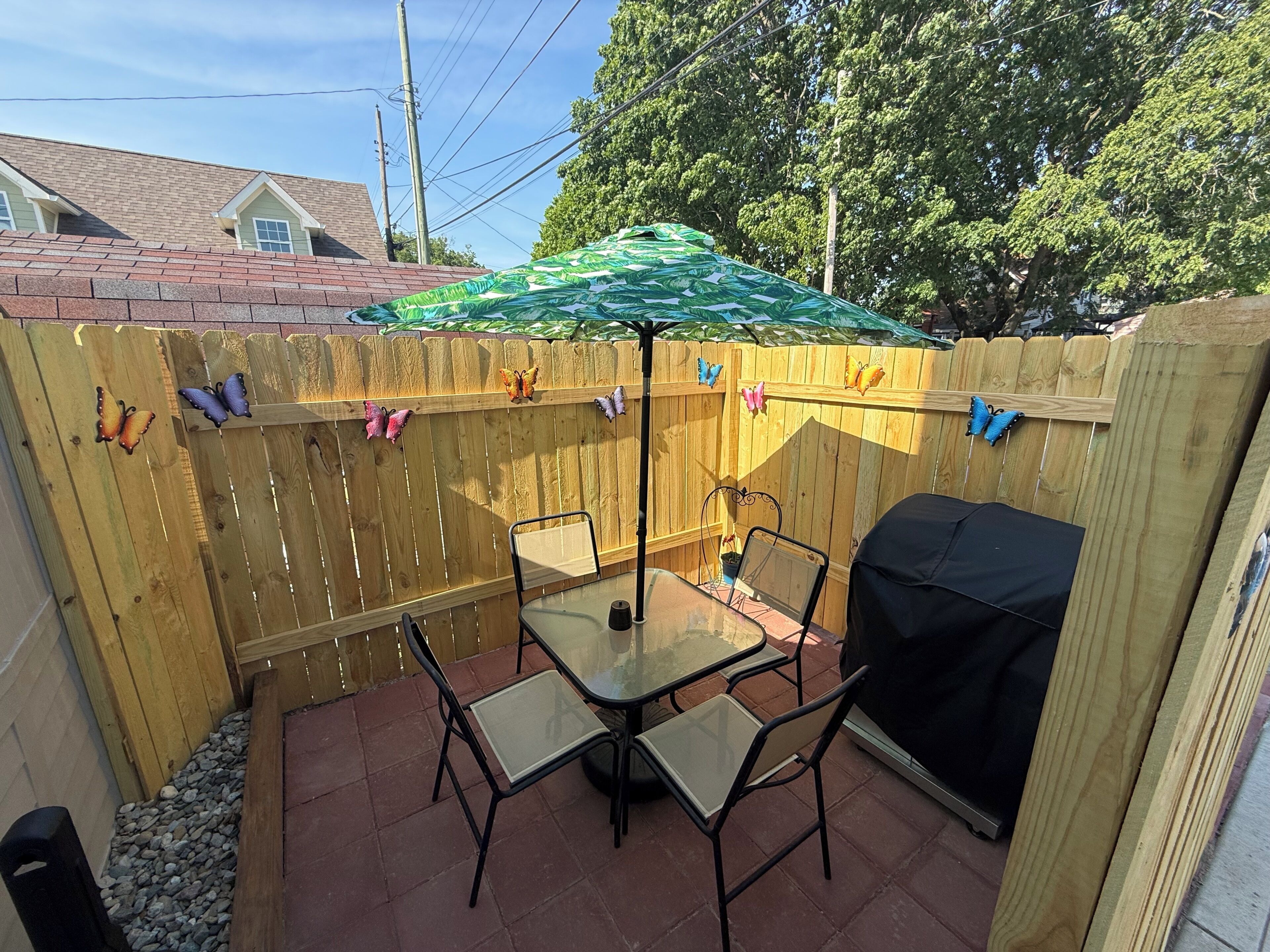 Eine Terrasse mit Tisch und Stühlen, einem überdachten Sonnenschirm und einem Holzzaun mit Schmetterlingsornamenten.