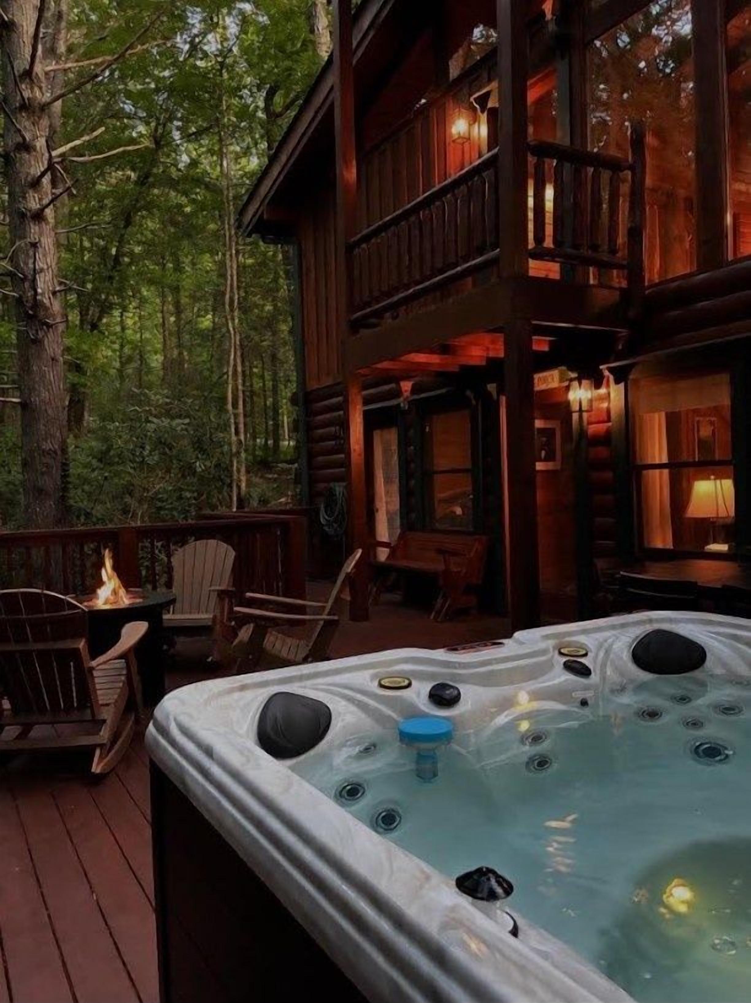Een houten chalet met een jacuzzi op een terras, omgeven door bomen.