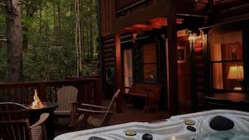 Uma cabana de madeira com hidromassagem em um deck rodeado por árvores.
