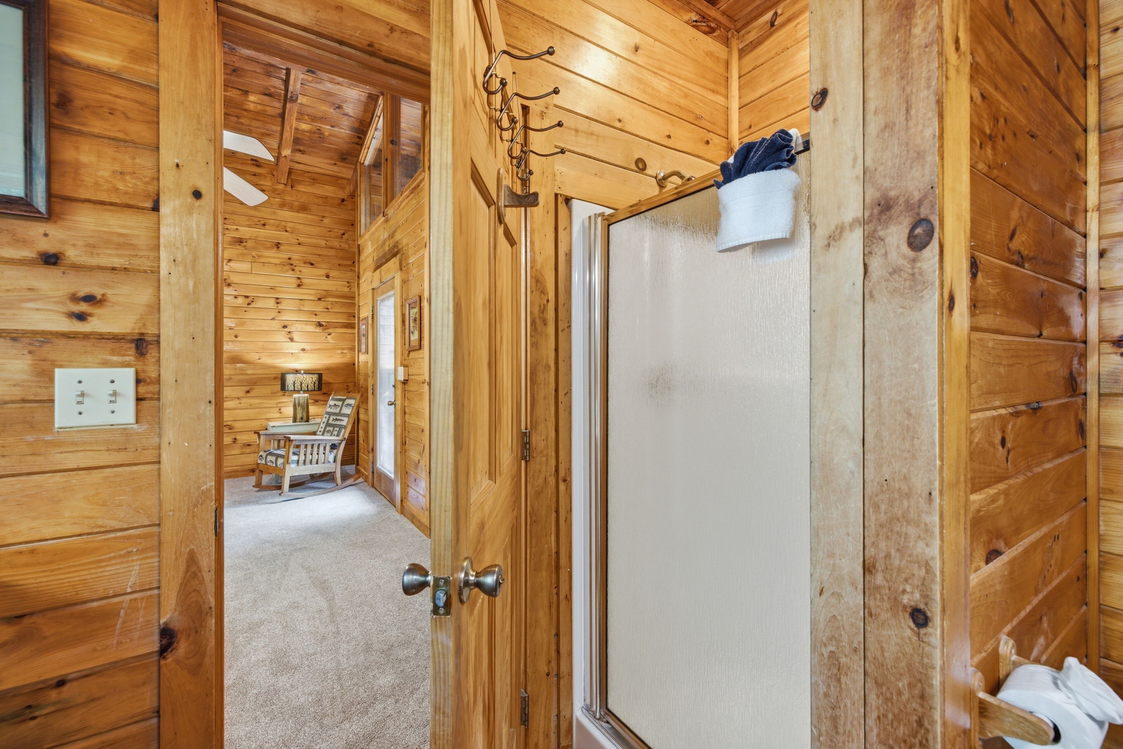A wooden interior with a door leading to a room with a bed, a chair, and a table.