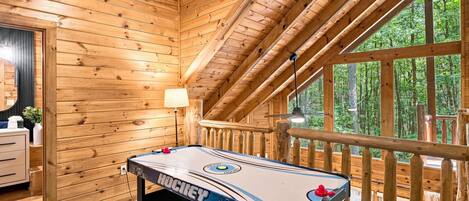 A wooden interior with a shuffleboard table, a lamp, and a view of the outdoors.