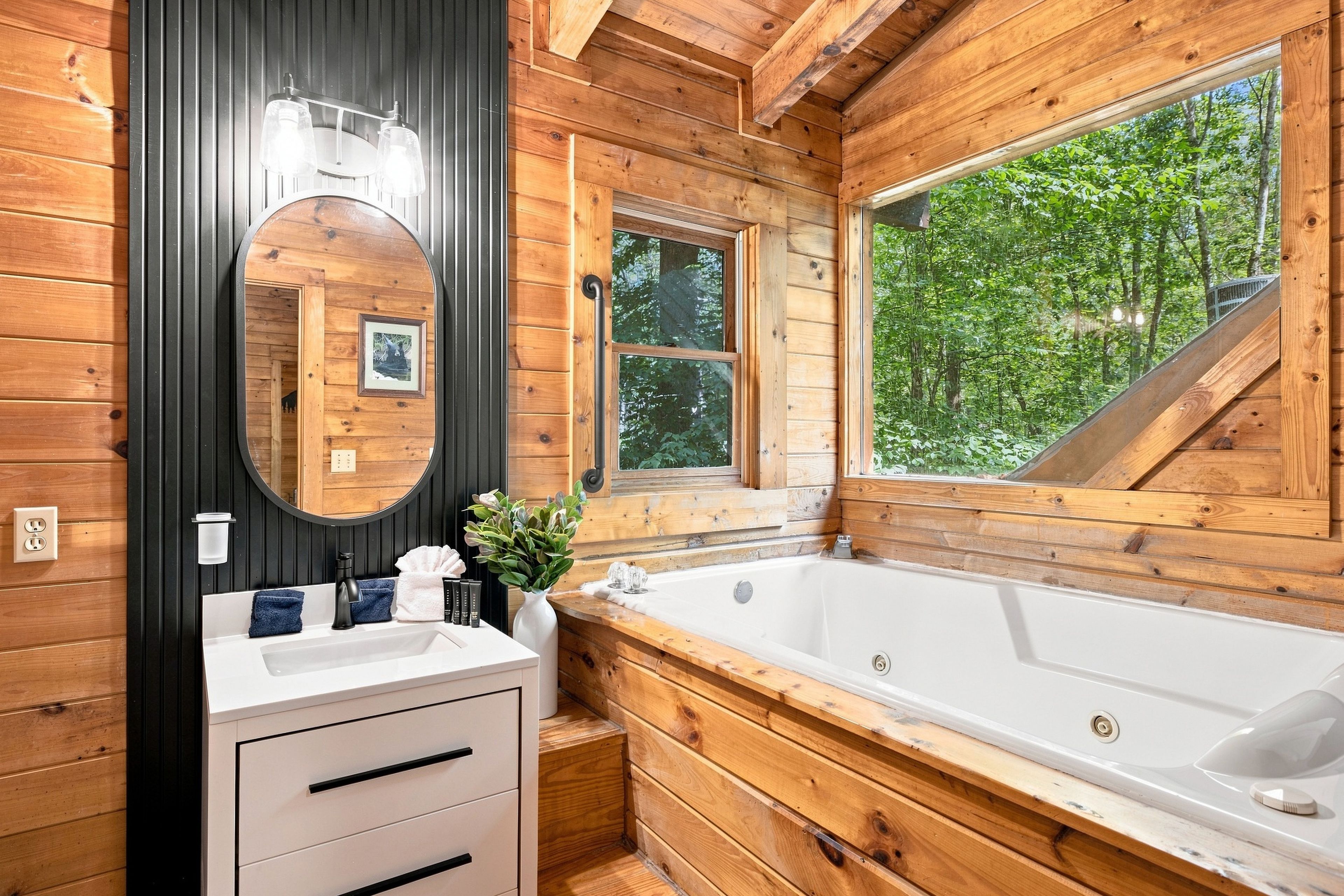 A wooden cabin bathroom with a large mirror, a window, a bathtub, and a sink.