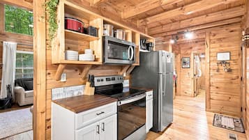 A compact kitchen with wooden walls, a built-in microwave, a stove, and a refrigerator.