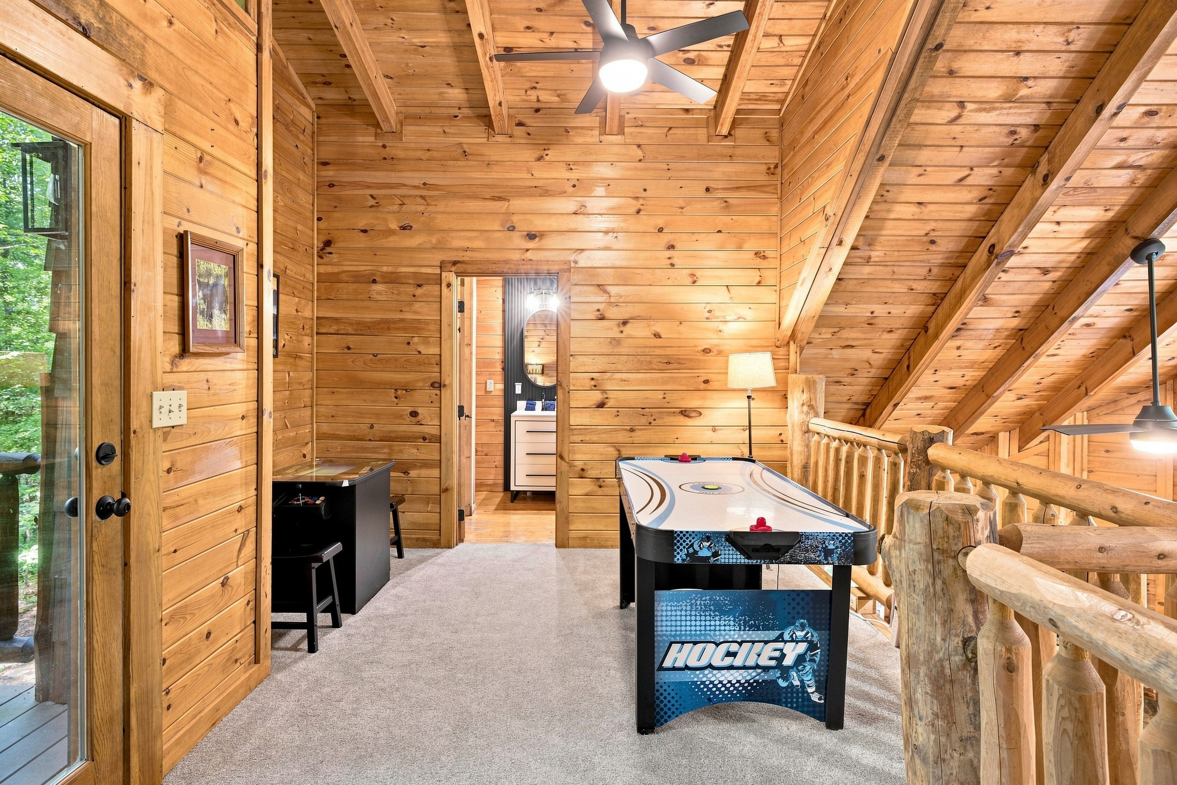 A wooden interior with a pool table, a ceiling fan, and a view of the outdoors.
