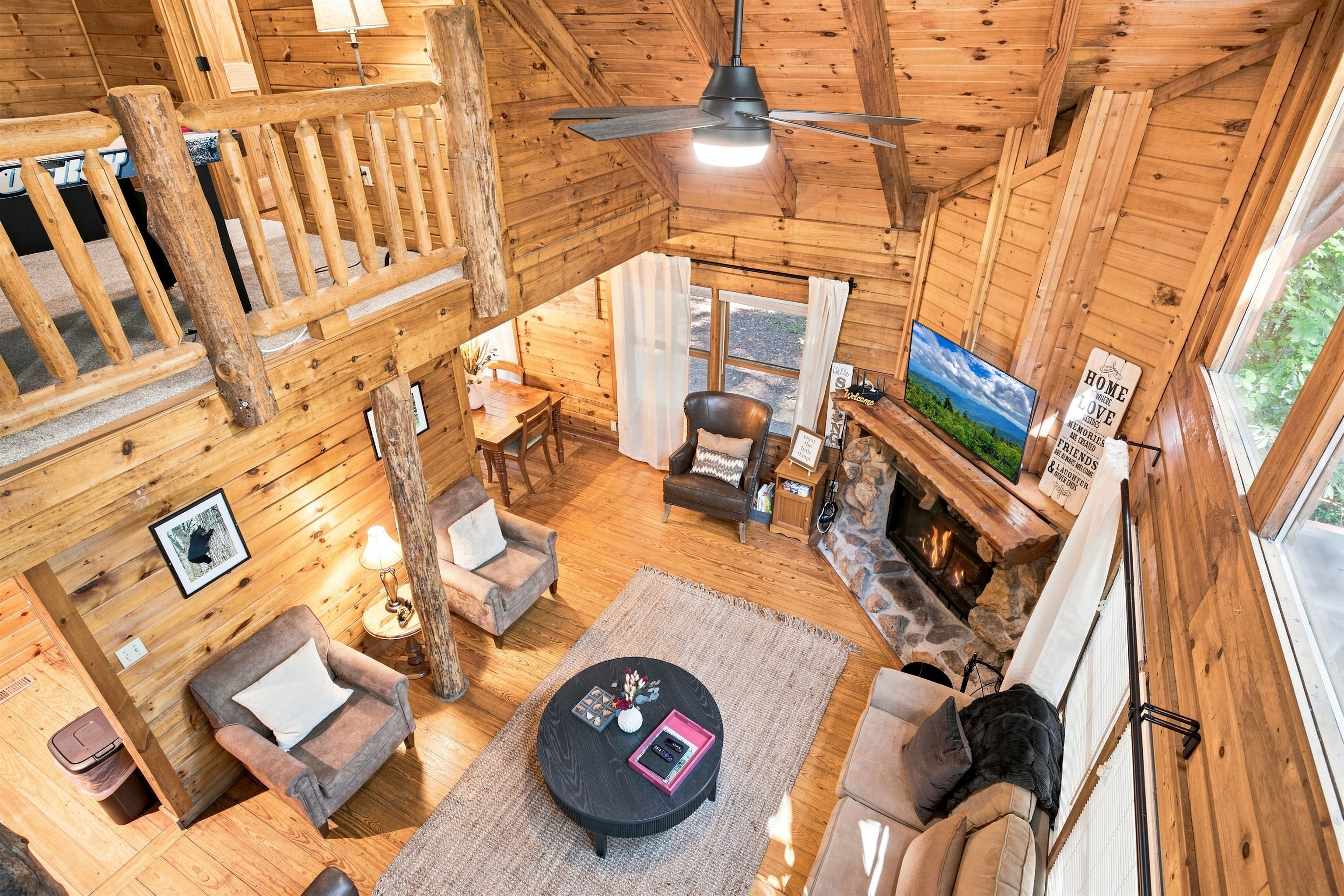 A wooden cabin interior with a dining area, seating, a fireplace, and a ceiling fan.
