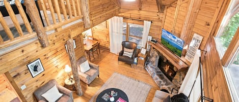 A wooden cabin interior with a dining area, seating, a fireplace, and a ceiling fan.