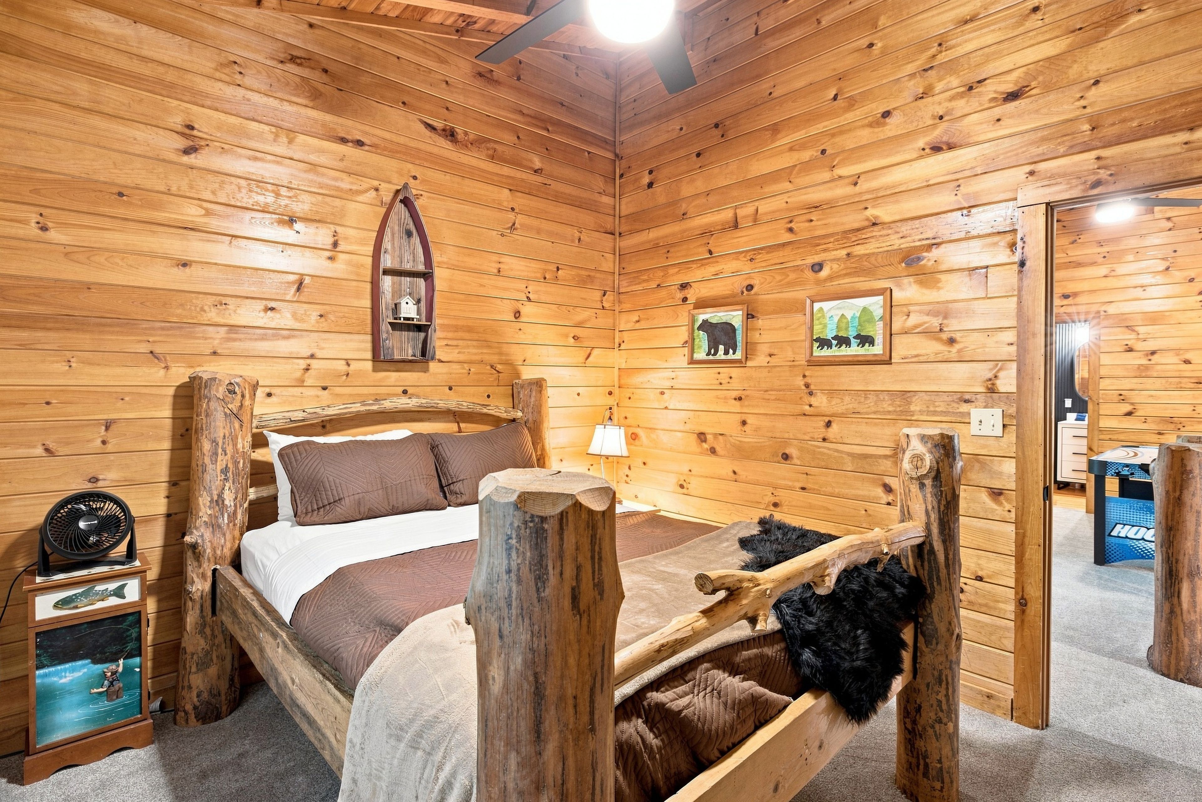 A wooden cabin bedroom with a bed, a fan, a lamp, and a framed picture on the wall.