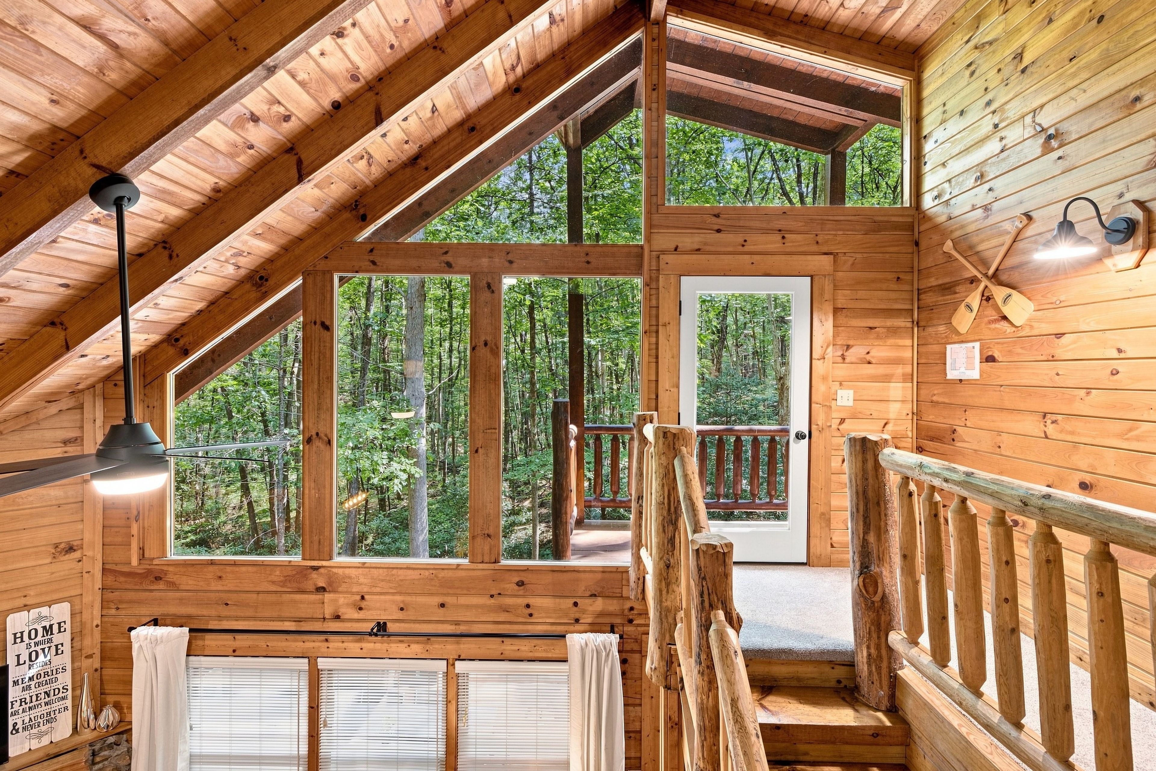 A wooden cabin with a loft bedroom, large windows, and a balcony overlooking a forest.