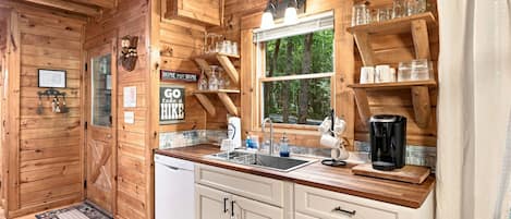 Interior de una cabaña de madera con cocina, que incluye un lavabo, armarios y una cafetera.