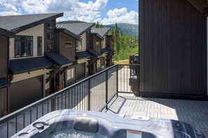 A hot tub on a deck with a view of a row of buildings and mountains. - Emerald Escape 3 Bedroom Home (Winter Park)