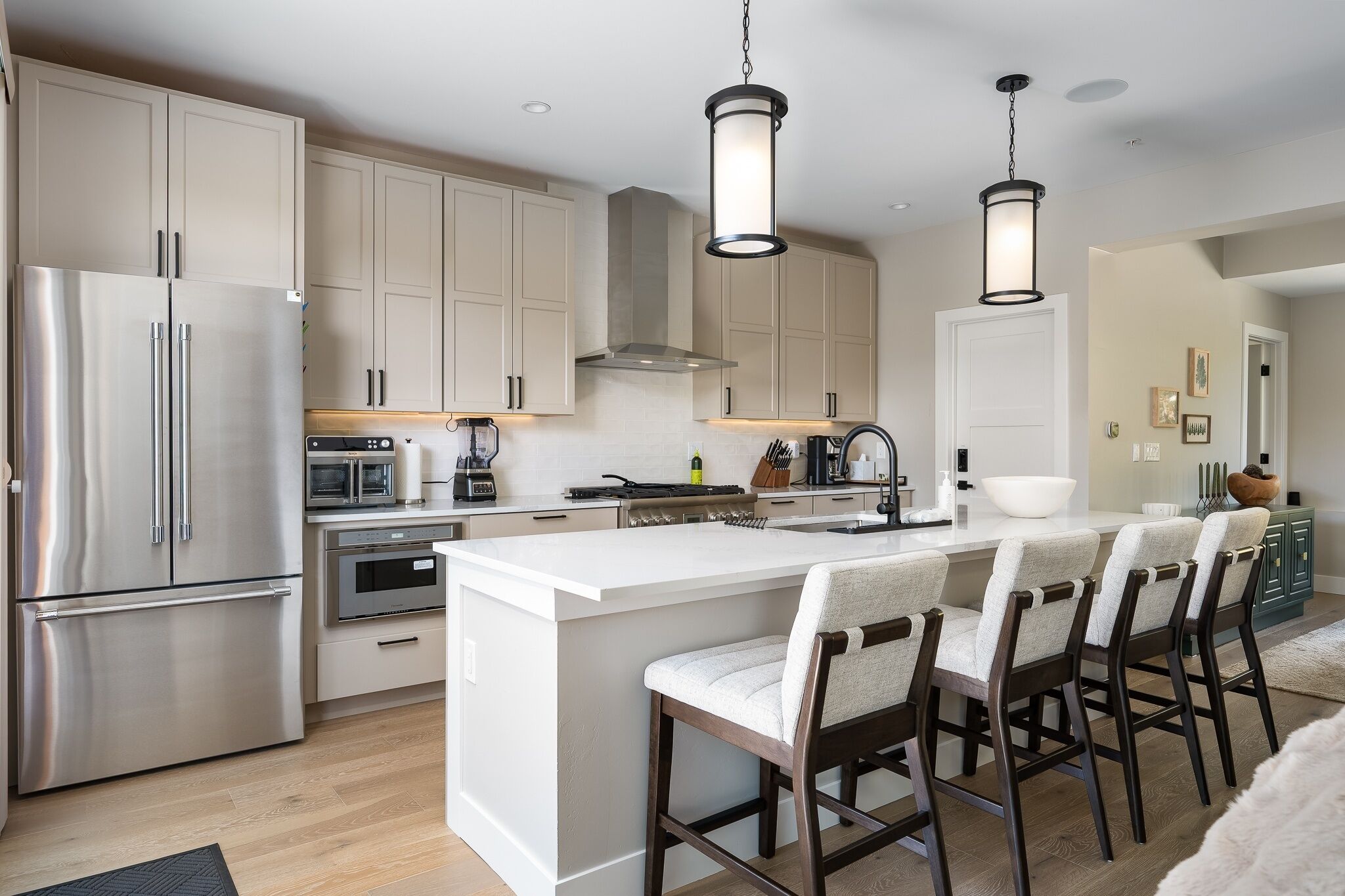 Una cocina moderna con electrodomésticos de acero inoxidable, una isla central con taburetes de bar e iluminación colgante.