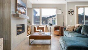 Ein modernes Wohnzimmer mit Kamin, großem Fenster, einer Couch, einem Couchtisch und einem an der Wand montierten Fernseher.