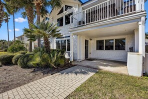 A two-story house with a covered front porch, a balcony, and a well-maintained garden with palm trees and shrubs. - 733b Tarpon Avenue 3 Bedroom Apts (Fernandina Beach)