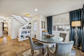 A dining area with a round glass table, grey upholstered chairs, a staircase with white railings, and a chandelier. - 733b Tarpon Avenue 3 Bedroom Apts (Fernandina Beach)