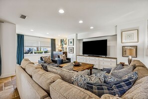 A living room with a sectional sofa, a coffee table, a flat-screen TV, and artwork on the walls. - 733b Tarpon Avenue 3 Bedroom Apts (Fernandina Beach)