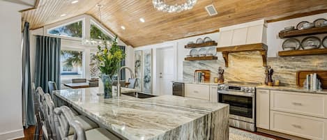 A modern kitchen with a marble island, wooden ceiling, and built-in shelving.