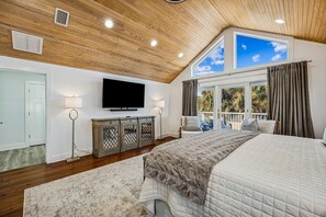 Une chambre avec un plafond en bois, un téléviseur à écran plat, un lit recouvert d’une couverture moelleuse, une table de chevet et une vue sur l’extérieur par une fenêtre.