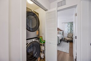 A laundry room with two washing machines, a drying rack, and a storage shelf with laundry items. - 733a Tarpon Avenue 3 Bedroom Apts (Fernandina Beach)