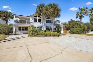 A two-story house with a balcony, surrounded by palm trees and a gravel driveway. - 733a Tarpon Avenue 3 Bedroom Apts (Fernandina Beach)