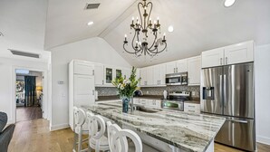 Una cocina moderna con armarios blancos, una isla de mármol, electrodomésticos de acero inoxidable y una lámpara de araña.