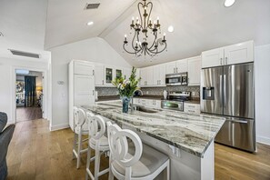 A modern kitchen with white cabinetry, a marble island, stainless steel appliances, and a chandelier. - 733a Tarpon Avenue 3 Bedroom Apts (Fernandina Beach)