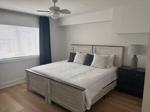 Ein Schlafzimmer mit einem Bett, einem Nachttisch, einer Lampe, einem Deckenventilator und einem Fenster mit Vorhängen.