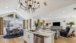 Una cocina moderna con una isla central, comedor con sillas y sala de estar con sofá y televisor.