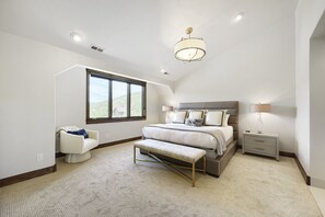 Ein Schlafzimmer mit einem großen Bett, einer Bank, einem Nachttisch und einem Fenster mit Aussicht.