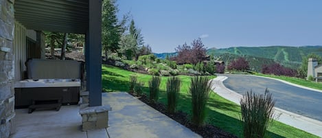 Un espacio al aire libre techado con un jacuzzi, un banco de piedra y vistas a un jardín ajardinado y una carretera.