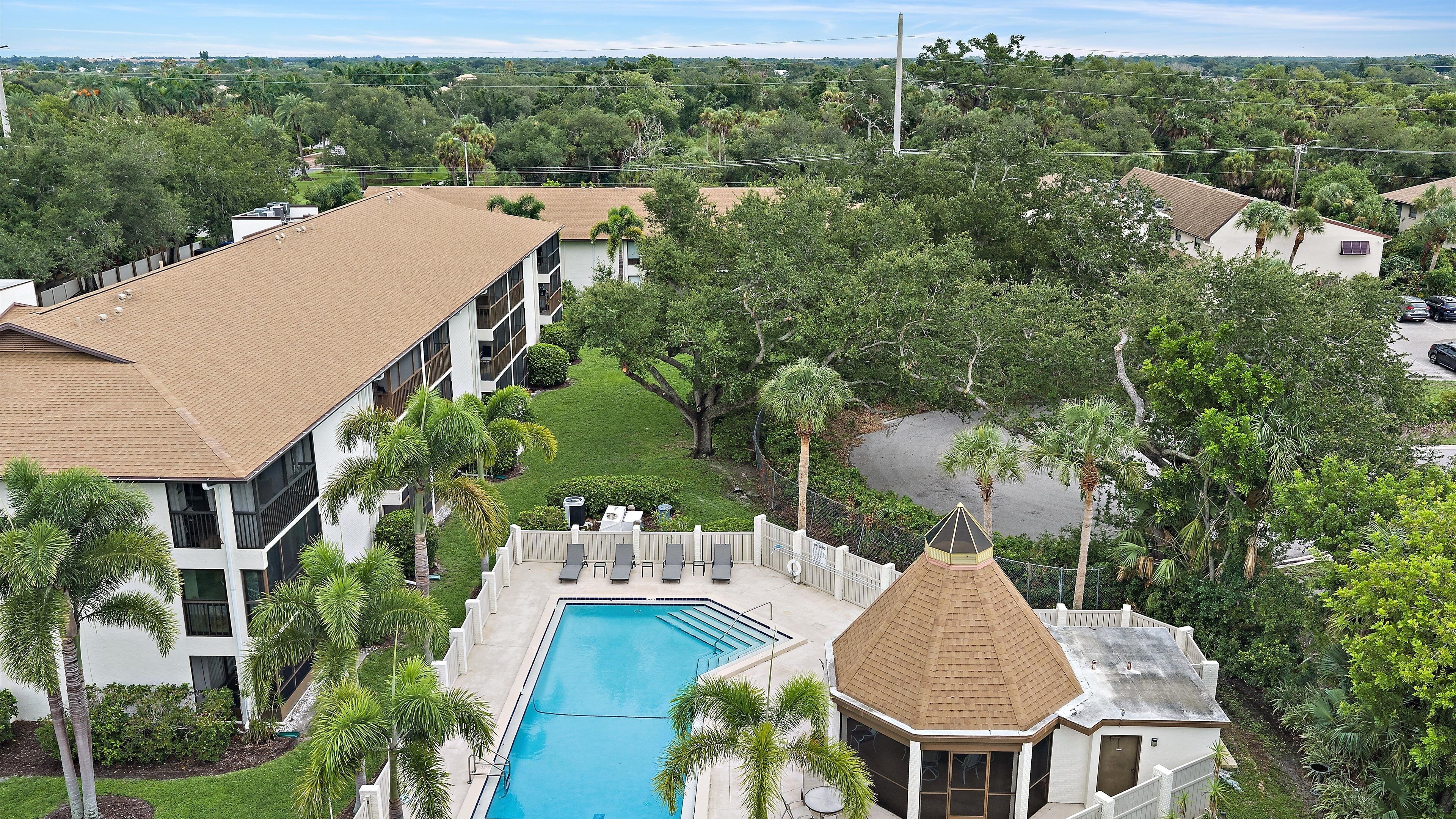 A residential building with a swimming pool, surrounded by lush greenery and palm trees.