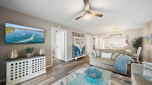 A living room with a TV, a van-shaped bookshelf, a ceiling fan, and a dining area. - Fort Goyastein South 2 Bedroom Condo (Sarasota)