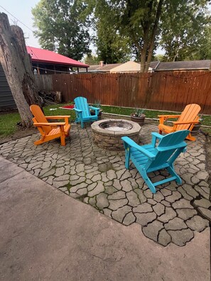 Eine Terrasse mit Adirondack-Stühlen und einer Feuerstelle.