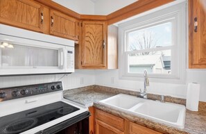 A kitchen with wooden cabinets, a white microwave, a stove, and a sink. - Chickasaw Chill House - Sleeps 6 - Fire Pit (Lakeview)