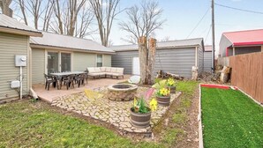Een achtertuin met een terras van natuursteen, buitenmeubilair, een vuurkorf en potplanten.