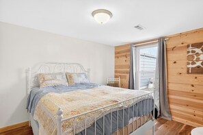 Ein Schlafzimmer mit einem Metallbettgestell, einer gesteppten Bettdecke und einer Holzwandverkleidung.