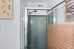 Eine Dusche mit Glastür, ein Lüftungsgitter darüber und ein gerahmtes Bild an der Wand.