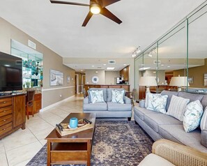 A modern living room with a sofa, coffee table, and a television. There is a kitchen area in the background. - Beach life at its finest Labor Day Rate direct gulf front, pool plus Hot Tub! (Destin)