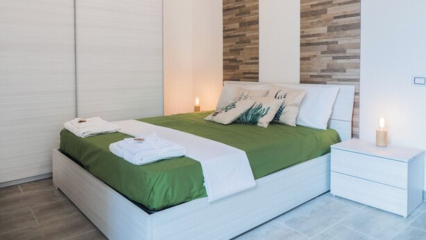 Un dormitorio moderno con cama, ropa de cama verde y blanca, una mesita de noche y un panel de madera decorando la pared.