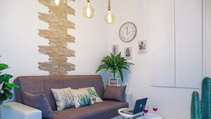 Una sala moderna con un sofá, una mesita con una computadora portátil y vasos, un cactus y un reloj de pared.