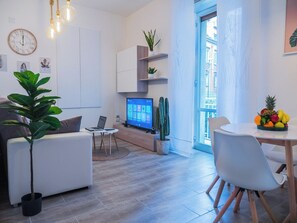 Una sala de estar moderna con un televisor de pantalla plana, una mesa de comedor con sillas, una planta en maceta y un cactus.