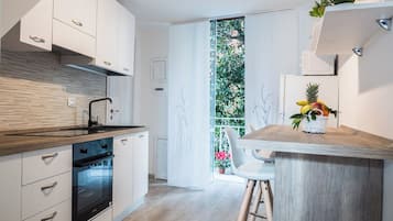 Una cocina moderna con armarios blancos, encimera de madera y horno empotrado. Se aprecia una pequeña isla con una cesta de frutas y una silla.