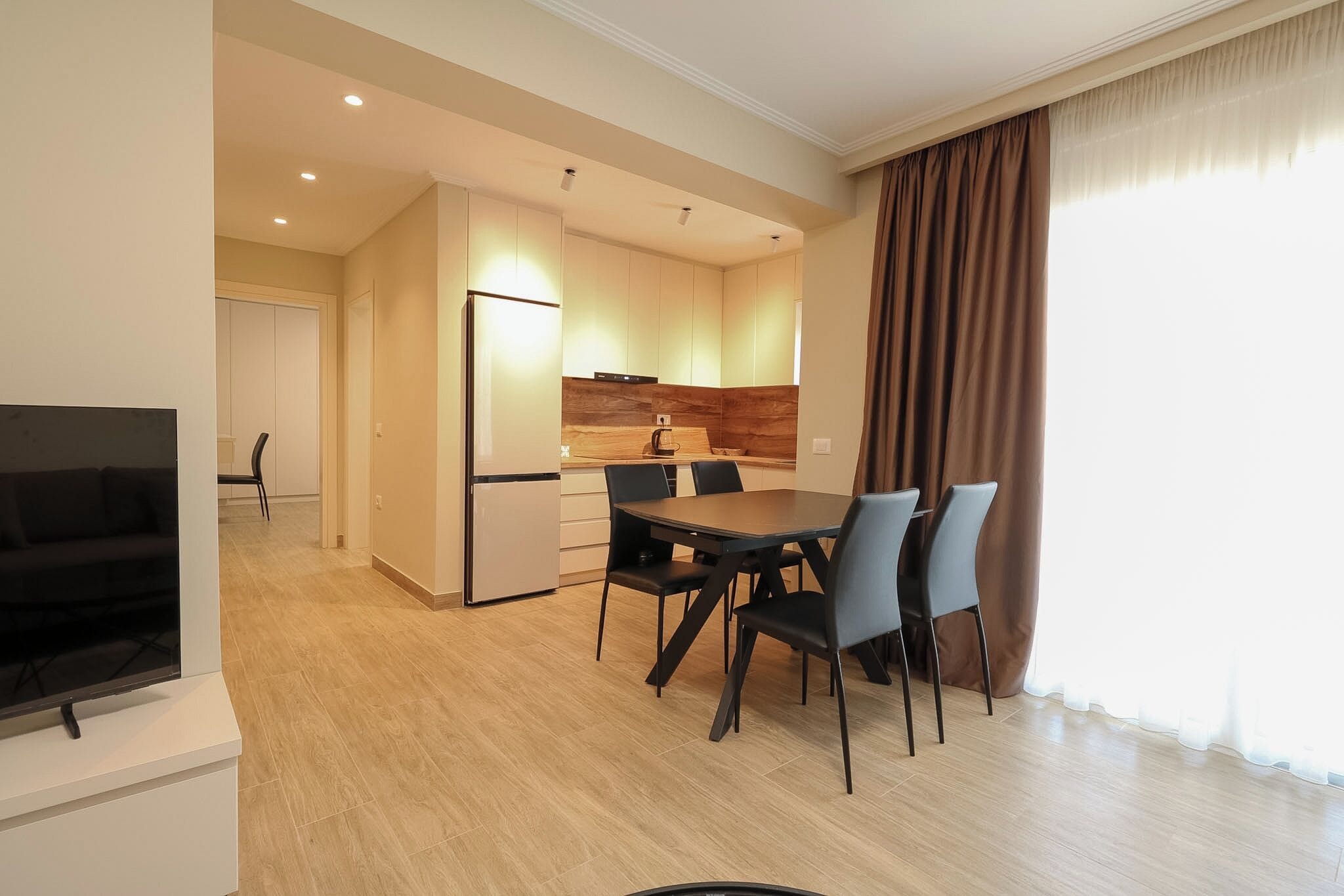 A modern apartment with a dining area, kitchen, and a TV.