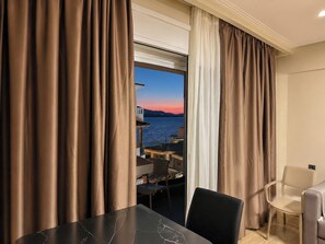 Una habitación de hotel con vista al mar al atardecer, una zona de comedor con sillas y mesas, y un sofá.