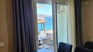 A room with a dining table and chairs, a sliding glass door leading to an outdoor area with a view of the sea and a building. - Milica Apartment (Ksamil)