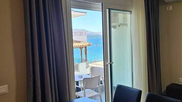 Una habitación con una mesa de comedor y sillas, una puerta corrediza de vidrio que da a un espacio exterior con vista al mar y un edificio.