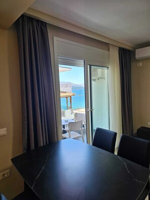 Ein Zimmer mit Esstisch und Stühlen, eine Schiebetür zu einem Außenbereich mit Blick auf das Meer und ein Gebäude.