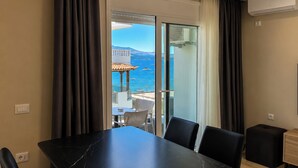 A hotel room with a dining table, chairs, a view of the sea, and a balcony with a table and chairs. - Milica Apartment (Ksamil)
