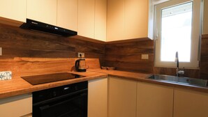 A modern kitchen with wooden cabinetry, a dishwasher, a coffee maker, and a window providing natural light. - Milica Apartment (Ksamil)