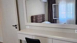A hotel room with a white desk, a black chair, a large mirror, and a window with curtains. - Milica Apartment (Ksamil)